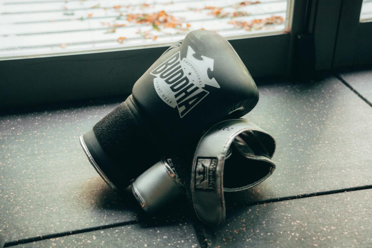 A pair of black boxing gloves lying on a gym floor near a window.