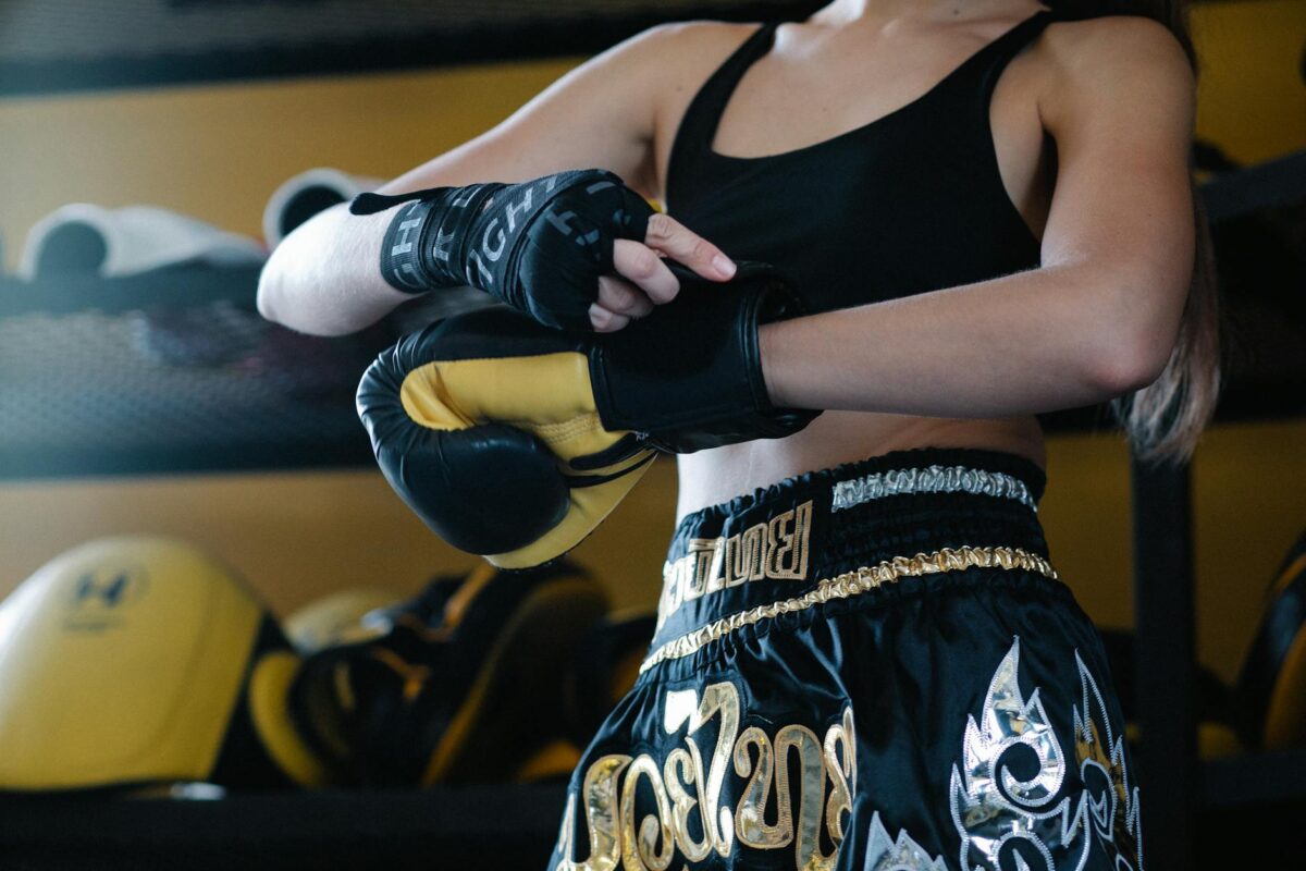Faceless crop sportswoman in dark sportswear fastening boxing glove on hand while preparing for training