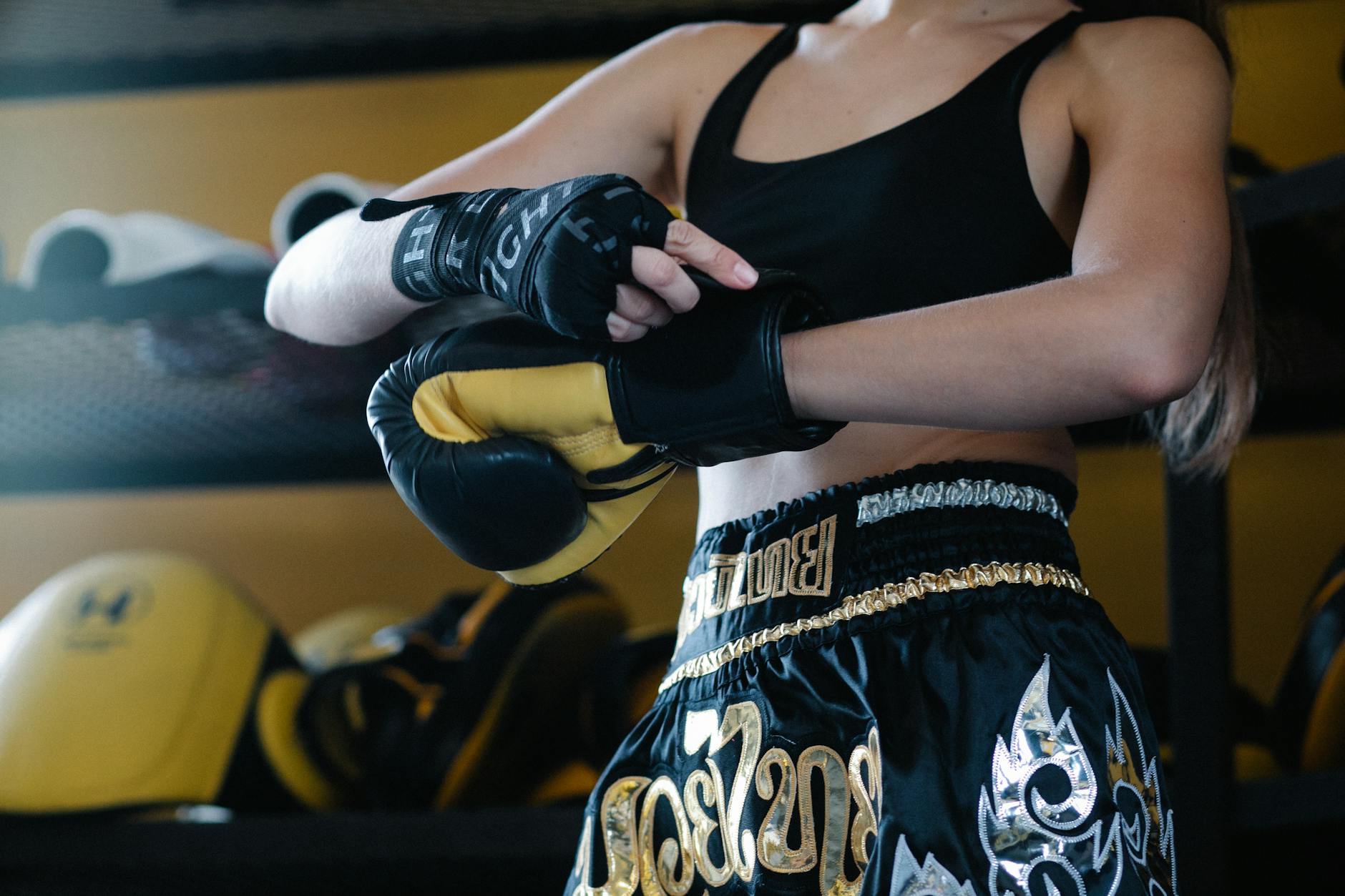 Faceless crop sportswoman in dark sportswear fastening boxing glove on hand while preparing for training